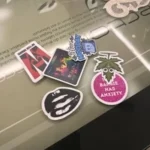 A cluster of diverse lifestyle stickers, including one that says "THIS BARBIE HAS ANXIETY," resting on a glass desk with a reflective surface.
